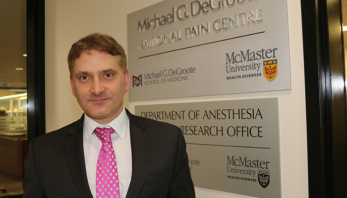 Jason Busse, wearing a pink polkadot neck tie, standing in front of the Michael G. DeGroote National Pain Centre.