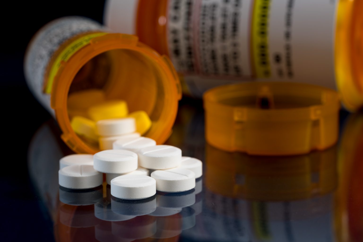 Yellow pill bottle on its side with white pills spilling out onto a black surface.