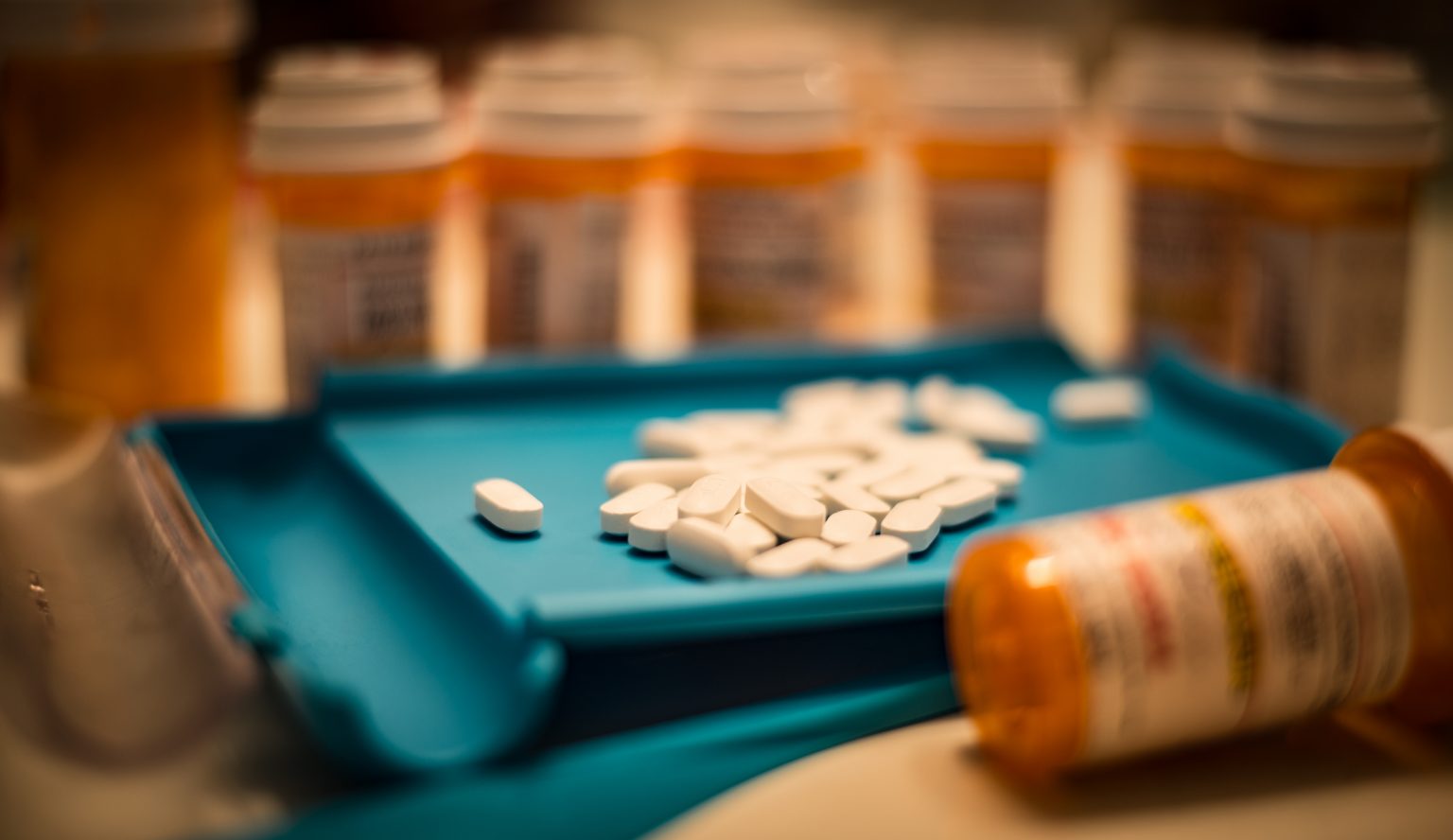 Photo of white pills scattered on a pill counting tray, next to an open bottle.